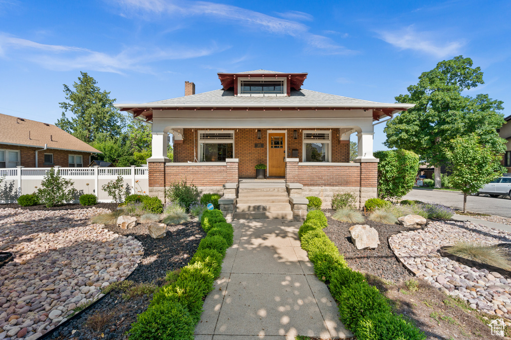 View of front of house featuring a porch, brick siding, and a chimney