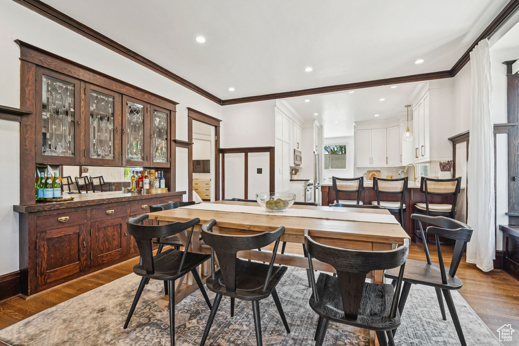 Dining area with crown molding, dark wood-style floors, recessed lighting, and bar area