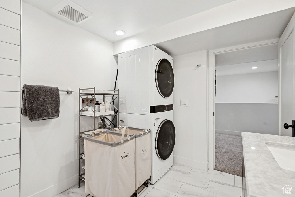 Laundry room featuring stacked washer / dryer, light marble finish flooring, and recessed lighting