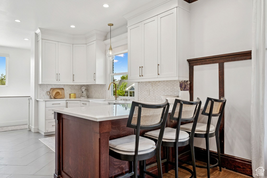 Kitchen featuring a breakfast bar, light countertops, white cabinetry, decorative backsplash, and recessed lighting
