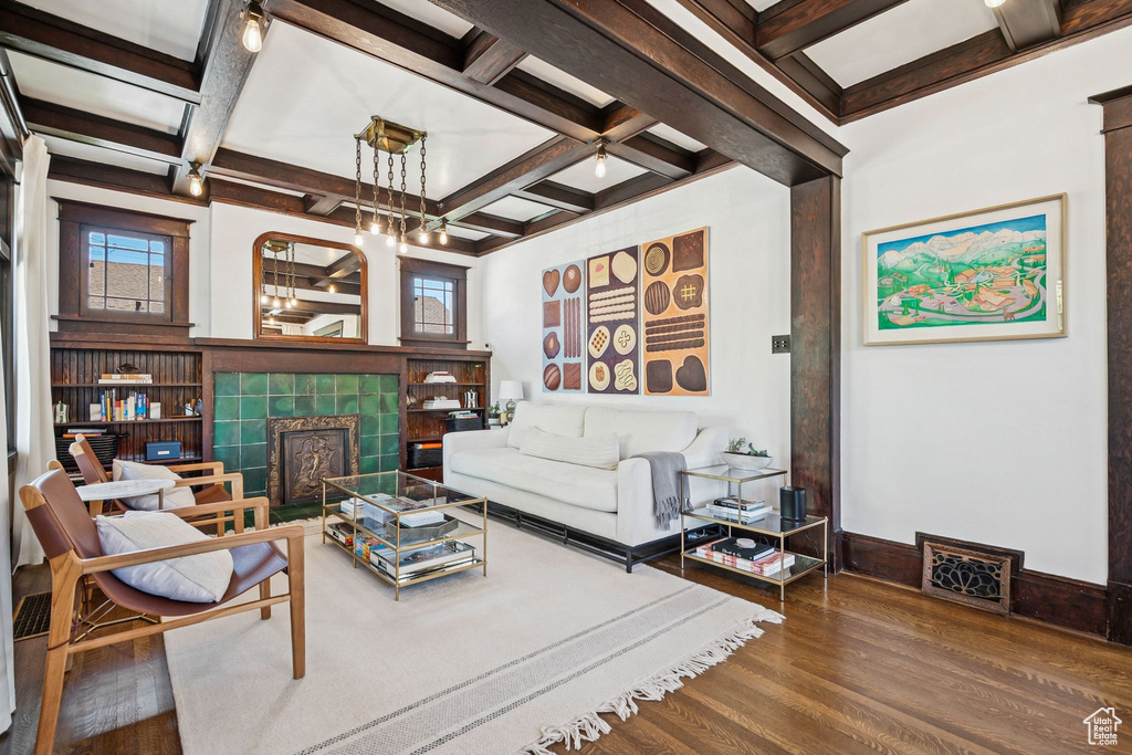 Living area featuring coffered ceiling, wood finished floors, beam ceiling, a tiled fireplace, and a chandelier