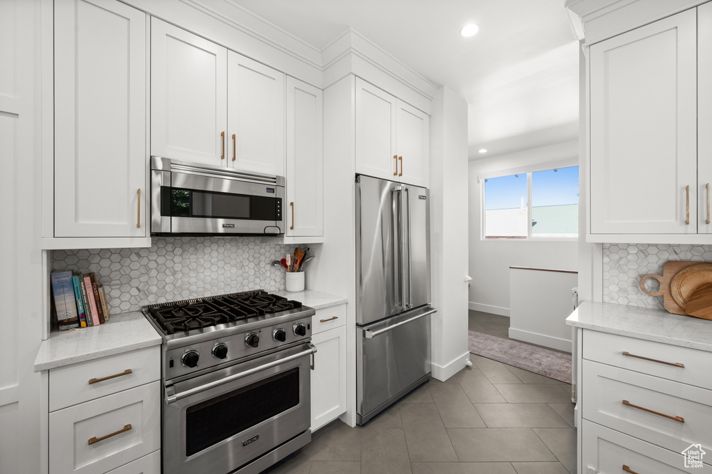 Kitchen with high end appliances, tasteful backsplash, white cabinetry, recessed lighting, and light tile patterned floors