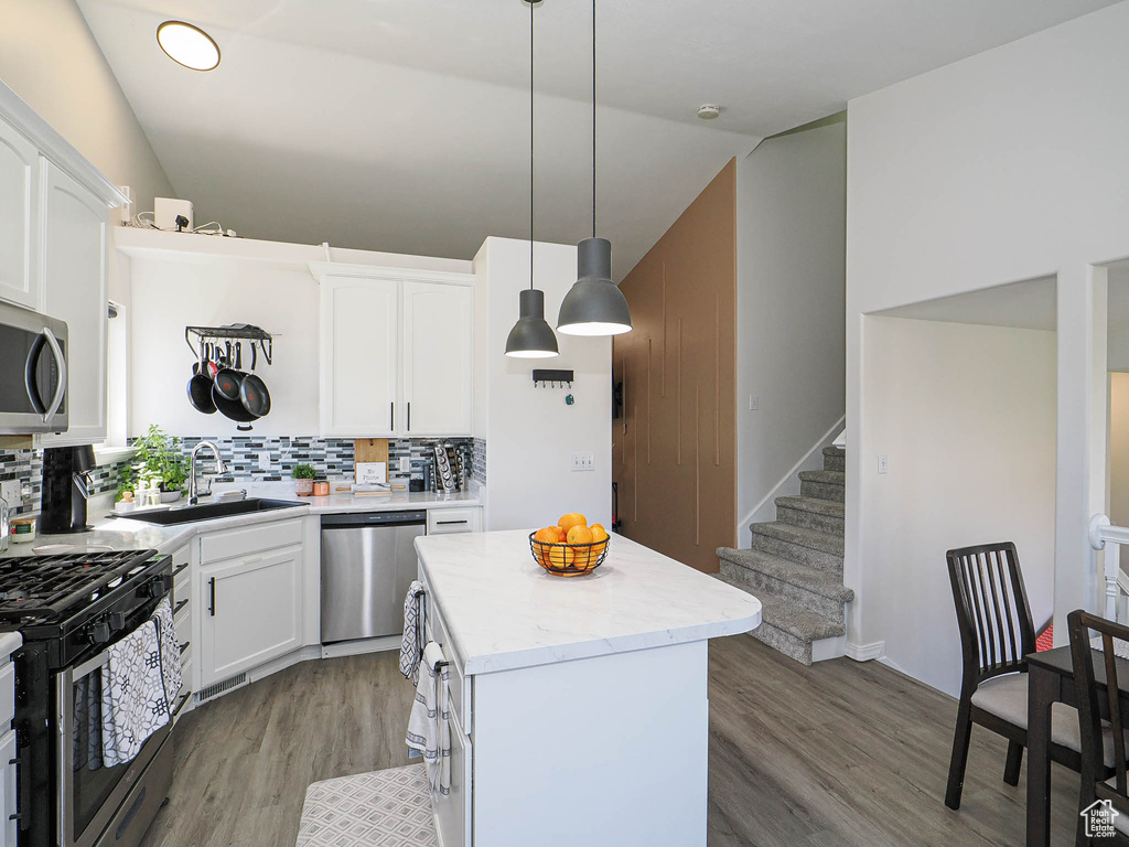 Kitchen featuring appliances with stainless steel finishes, vaulted ceiling, light wood finished floors, a kitchen island, and backsplash