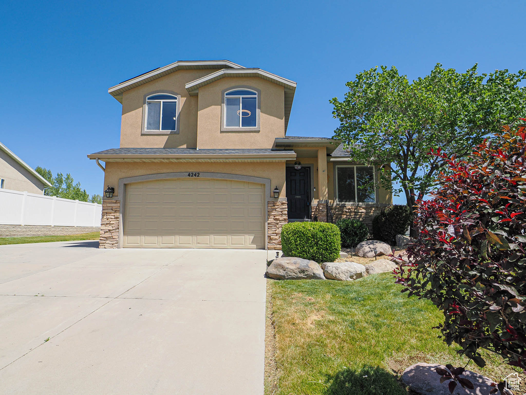 View of front of house with stone siding, stucco siding, a garage, and concrete driveway