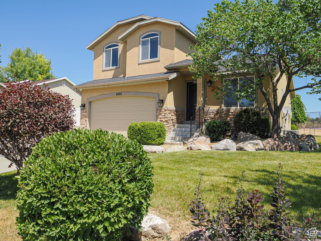 View of front of house with stucco siding, stone siding, an attached garage, and a front yard
