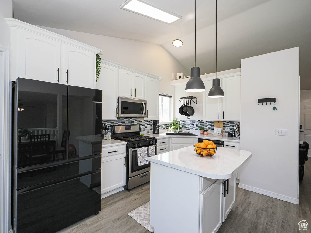 Kitchen featuring stainless steel appliances, white cabinetry, decorative backsplash, light countertops, and vaulted ceiling
