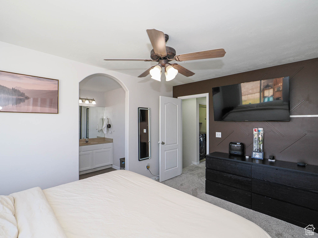 Bedroom with arched walkways, light colored carpet, ensuite bathroom, and ceiling fan