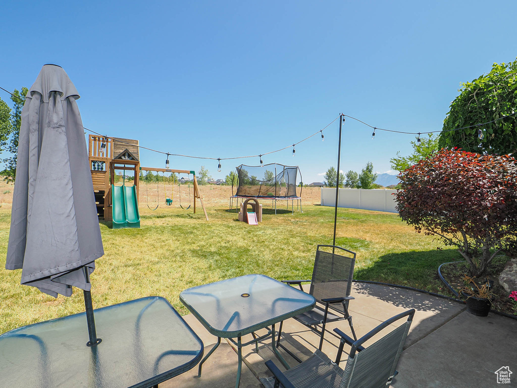 Fenced backyard featuring a playground, a trampoline, and a patio