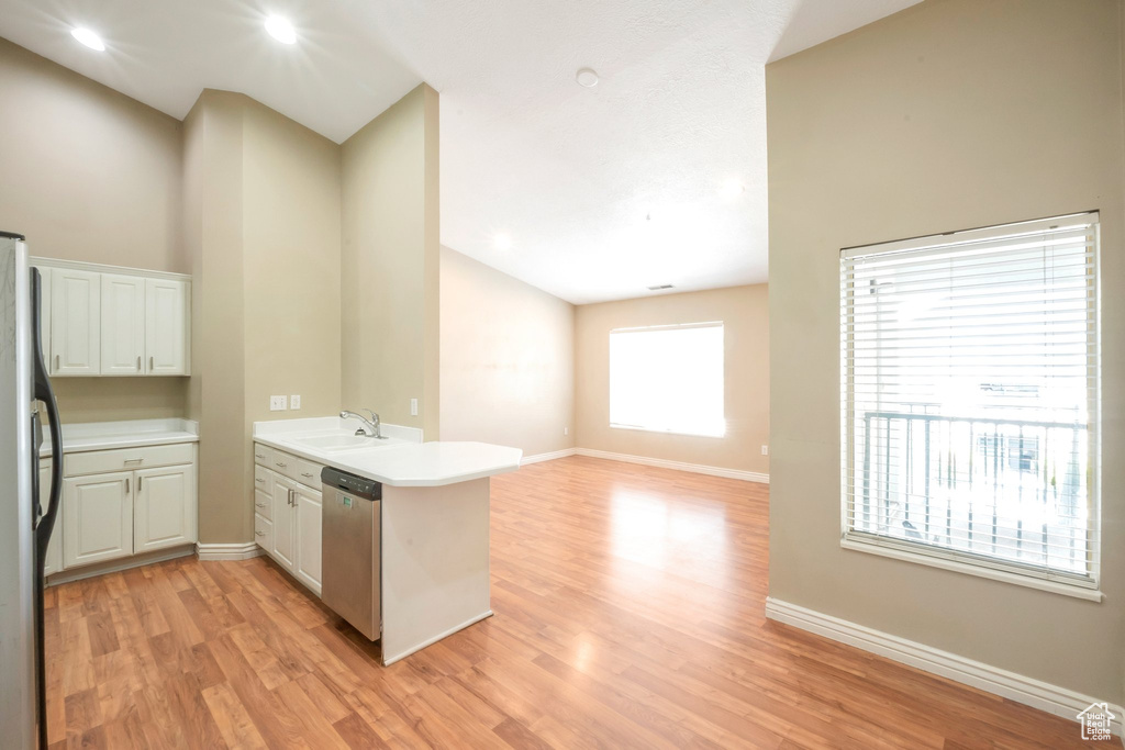 Kitchen with a peninsula, appliances with stainless steel finishes, light wood-style floors, light countertops, and white cabinetry