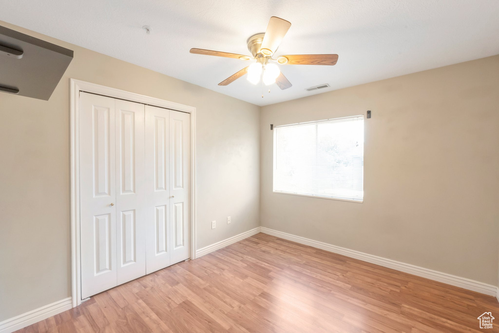 Unfurnished bedroom with light wood-style flooring, a closet, and a ceiling fan