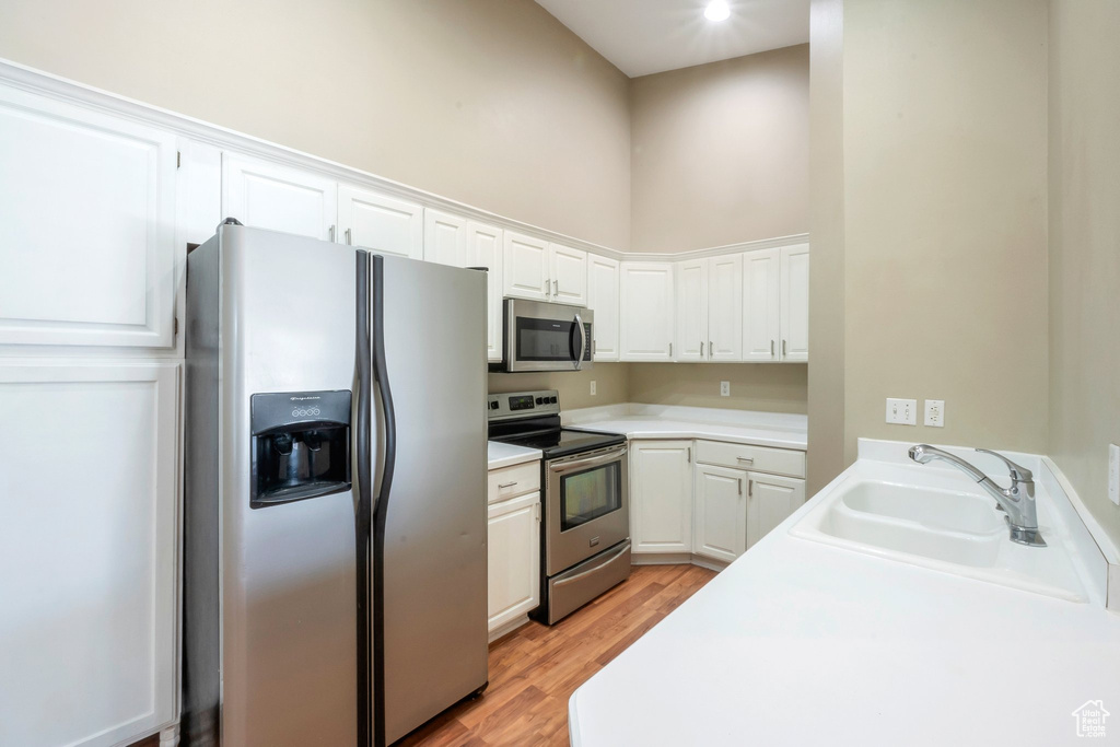 Kitchen featuring appliances with stainless steel finishes, light wood-type flooring, white cabinetry, light countertops, and a high ceiling