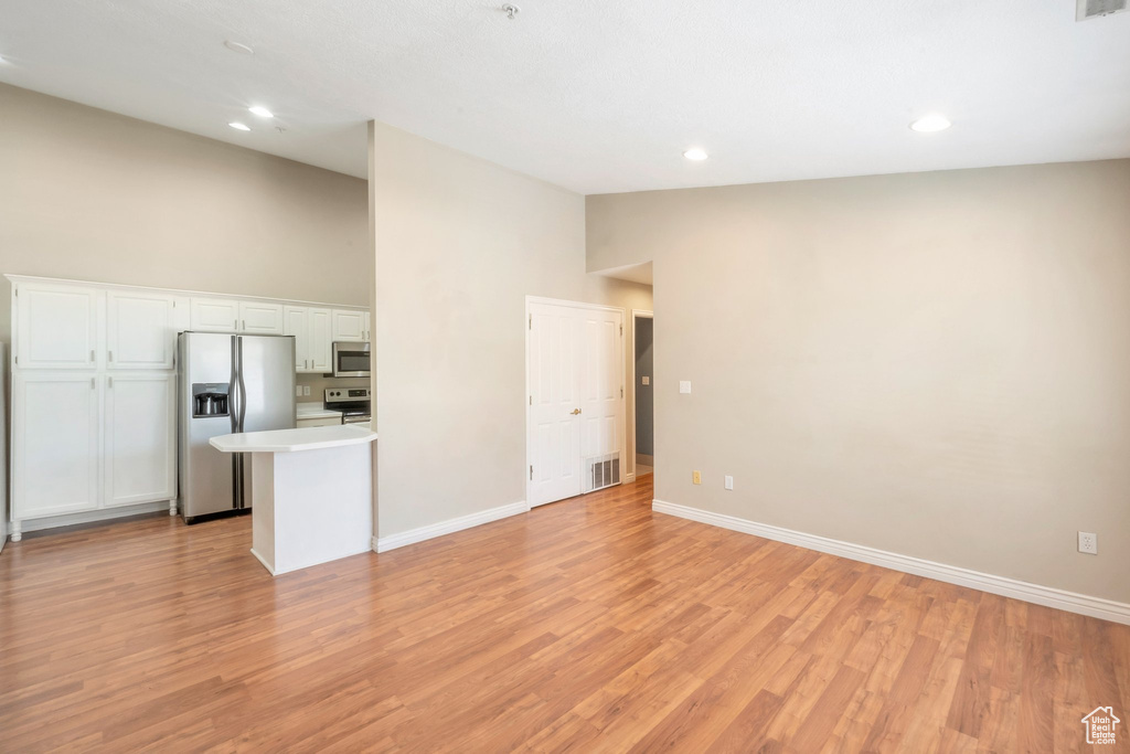 Unfurnished living room with light wood-type flooring, high vaulted ceiling, and recessed lighting
