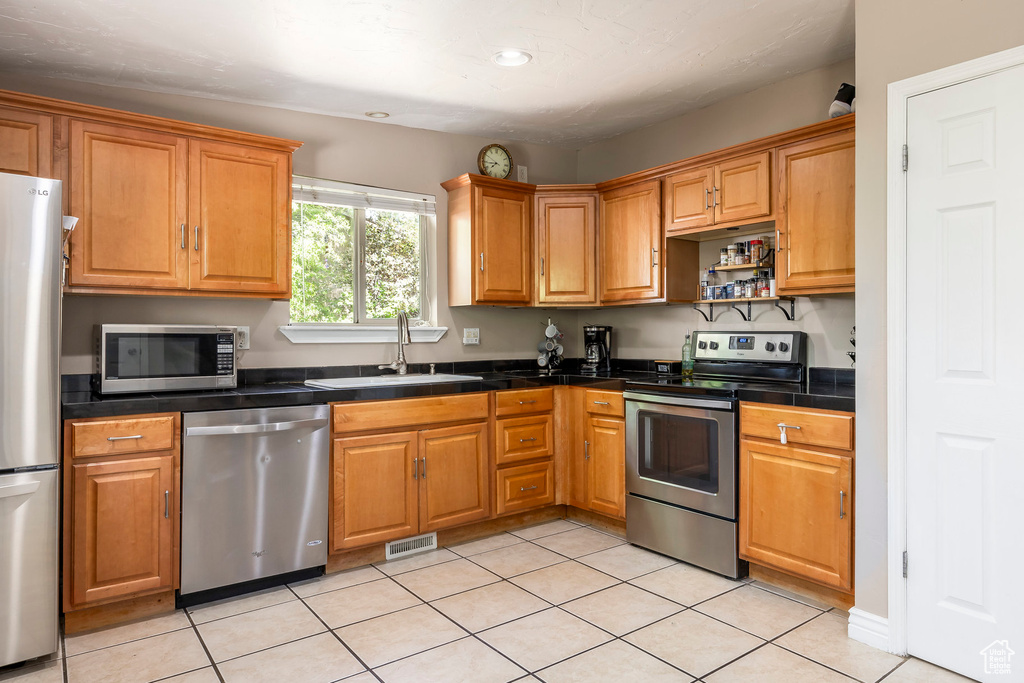 Kitchen with appliances with stainless steel finishes, light tile patterned floors, recessed lighting, brown cabinetry, and open shelves