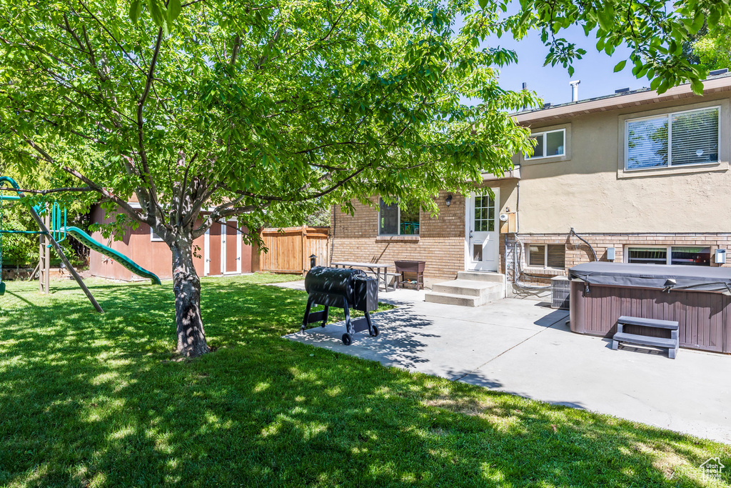 Fenced backyard featuring a hot tub, a patio area, a shed, and a playground