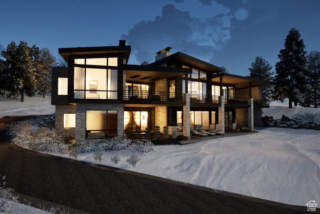 Snow covered house featuring a balcony and stone siding
