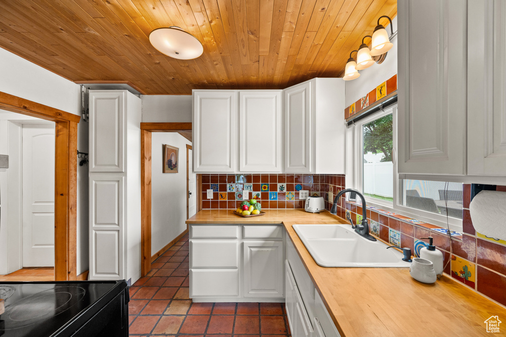 Kitchen with wood ceiling, backsplash, white cabinetry, tile patterned flooring, and electric range