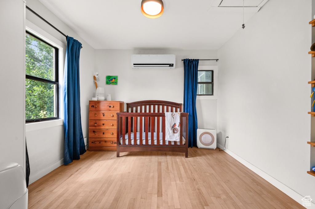 Bedroom with a wall mounted AC, attic access, light wood finished floors, and multiple windows
