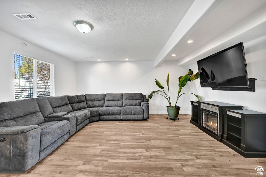 Living area featuring light wood finished floors, recessed lighting, a textured ceiling, and a glass covered fireplace