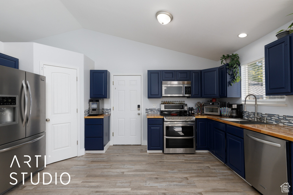 Kitchen featuring stainless steel appliances, butcher block countertops, blue cabinets, vaulted ceiling, and recessed lighting
