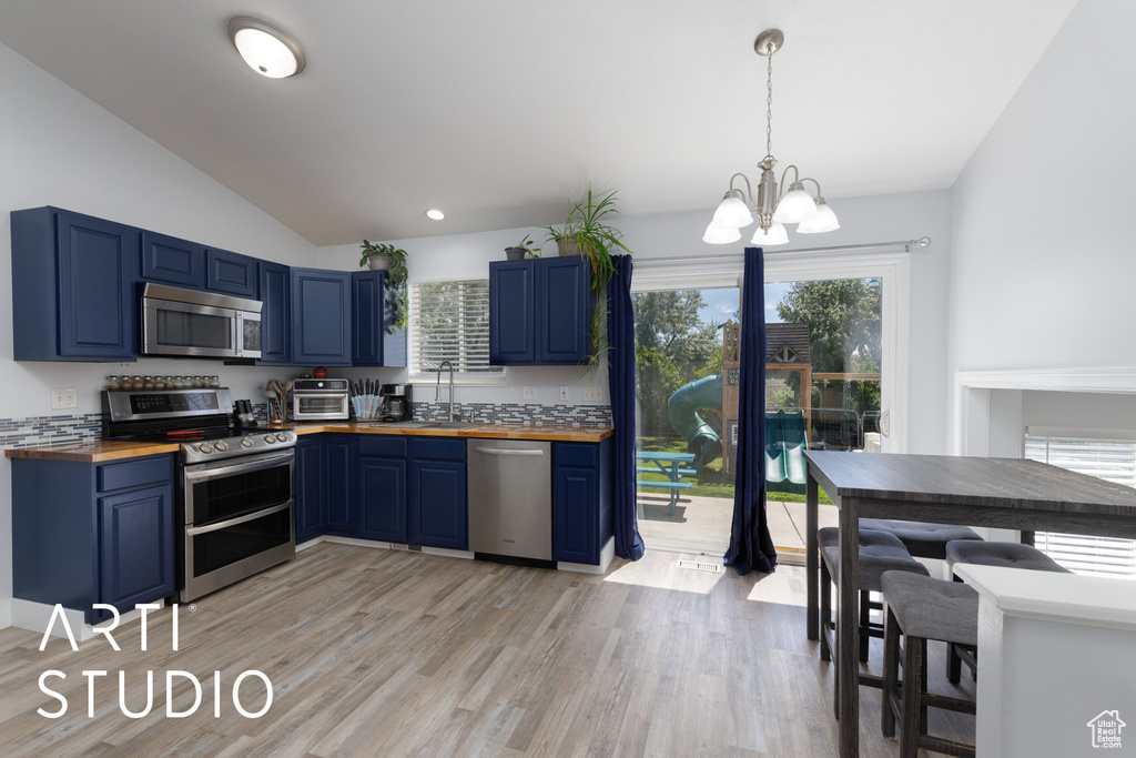 Kitchen with appliances with stainless steel finishes, butcher block countertops, blue cabinets, vaulted ceiling, and a chandelier