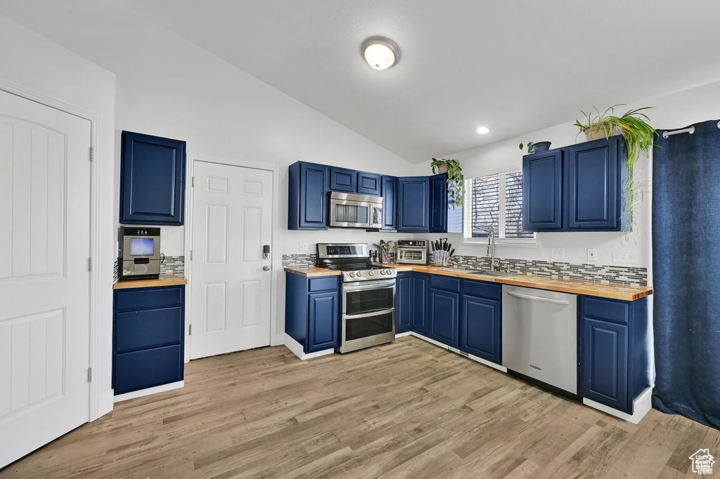Kitchen with appliances with stainless steel finishes, wooden counters, blue cabinetry, lofted ceiling, and light wood-style floors