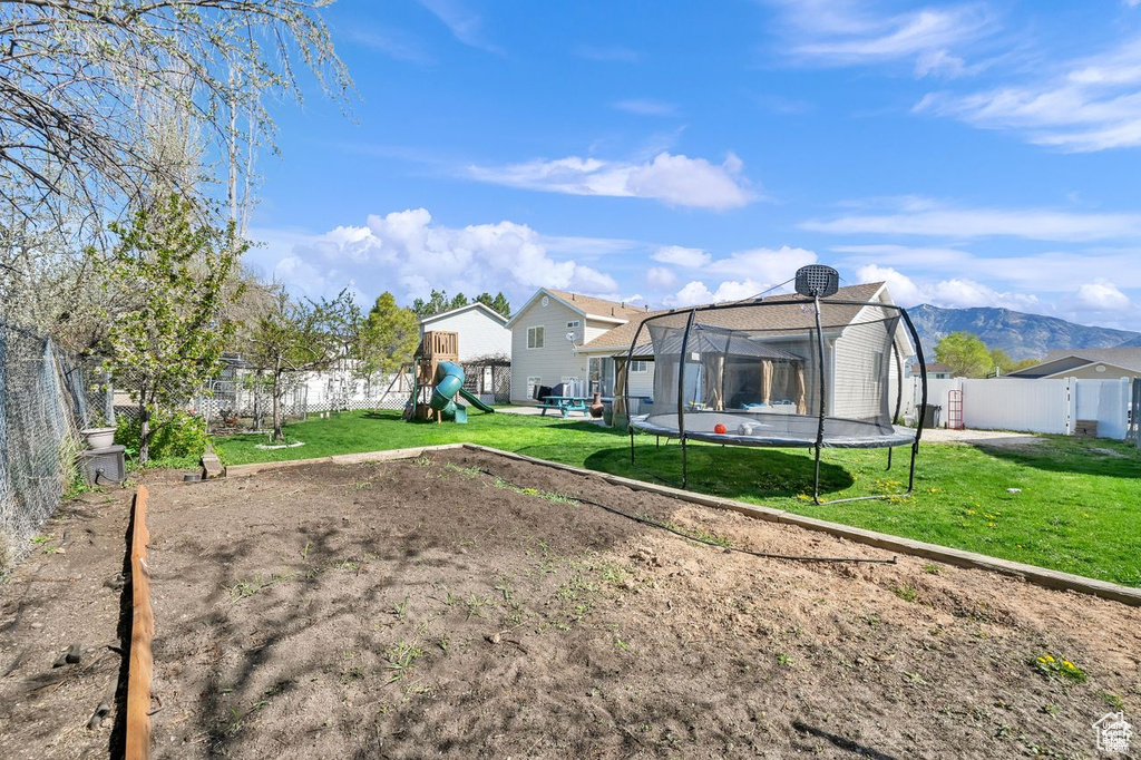 Fenced backyard featuring a trampoline and a playground