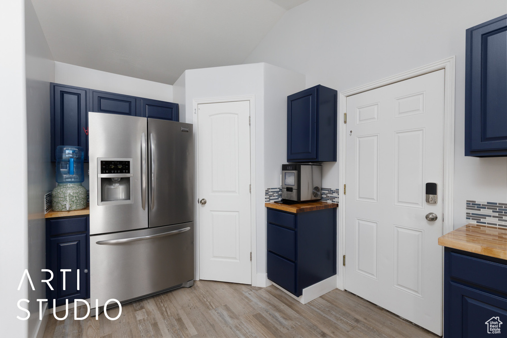 Kitchen featuring butcher block counters, stainless steel fridge, blue cabinets, and vaulted ceiling