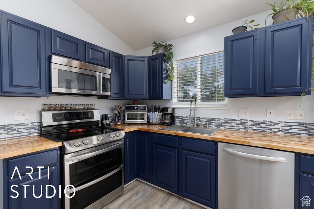 Kitchen with stainless steel appliances, wooden counters, blue cabinetry, lofted ceiling, and recessed lighting