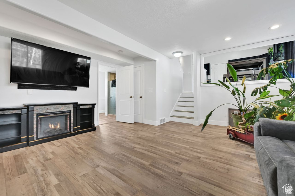 Living room with a stone fireplace, wood finished floors, stairway, and recessed lighting