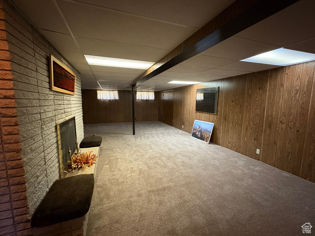 Basement with a paneled ceiling, carpet flooring, a fireplace, and wood walls