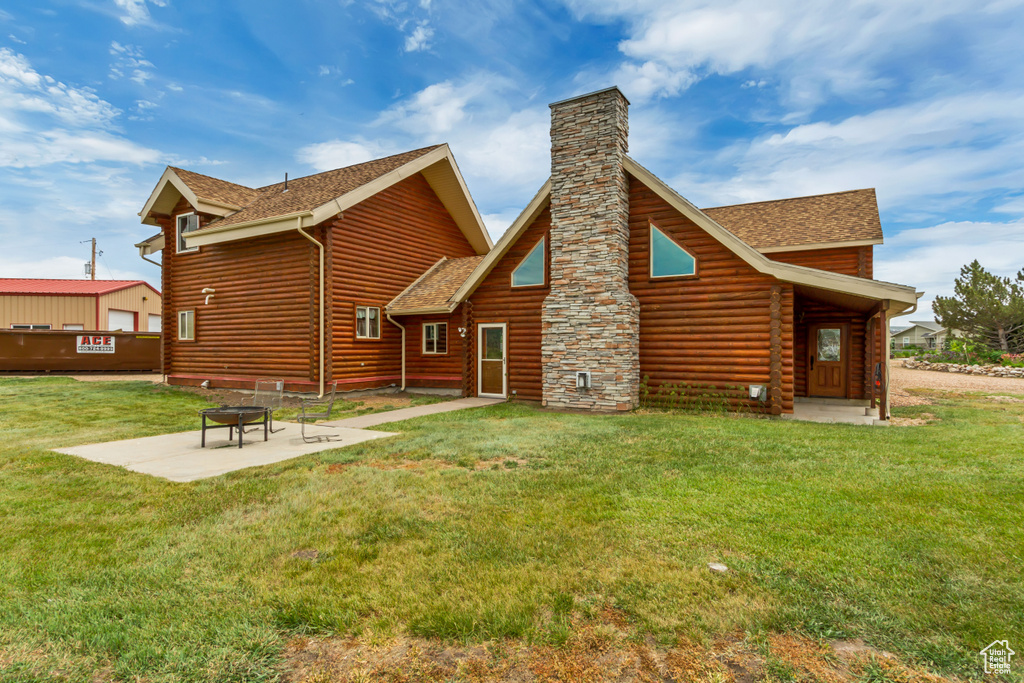 Rear view of property with an outdoor fire pit, roof with shingles, a chimney, a yard, and a patio