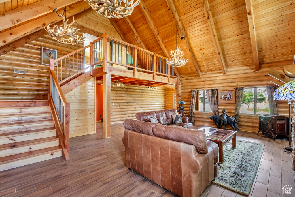 Living area featuring a chandelier, a wood stove, stairs, a wood ceiling with exposed beams, and log walls