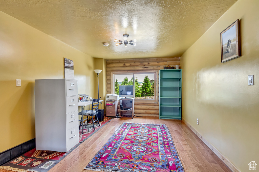 Office area with a textured ceiling, light wood-type flooring, a chandelier, and log walls