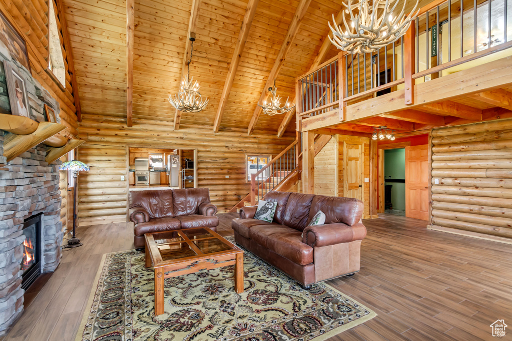 Living room with a chandelier, high vaulted ceiling, log walls, a wooden ceiling with exposed beams, and stairs