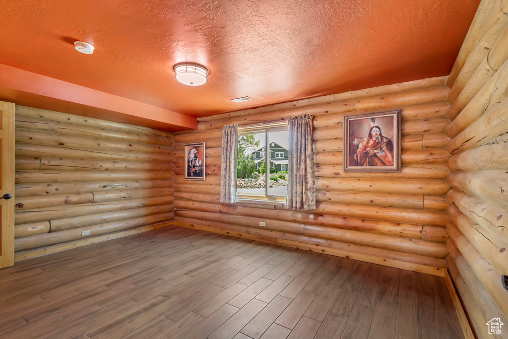 Empty room featuring a textured ceiling, wood finished floors, log walls, and a smoke detector
