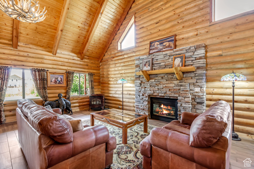 Living area featuring rustic walls, high vaulted ceiling, a wood ceiling with exposed beams, a stone fireplace, and a chandelier