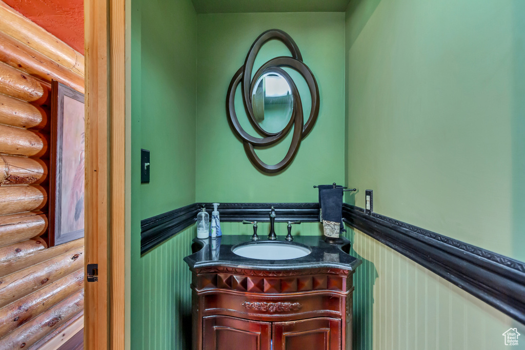 Half bath with log walls, vanity, and wainscoting