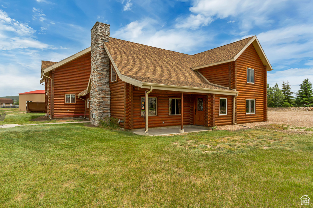 View of front of home with a shingled roof, log exterior, a front yard, a patio, and a chimney