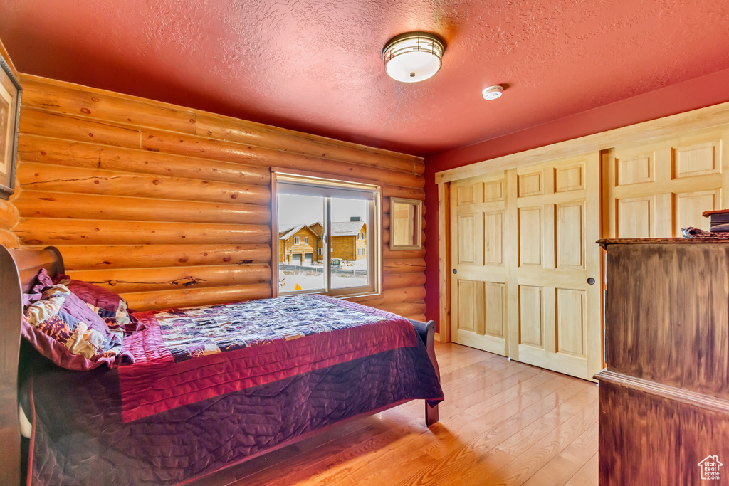 Bedroom with log walls, a textured ceiling, and wood finished floors