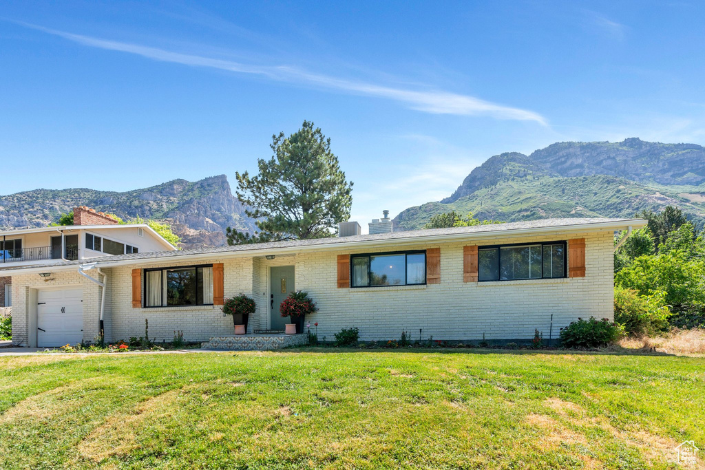 View of front of property with a mountain view, brick siding, a front lawn, a chimney, and a garage