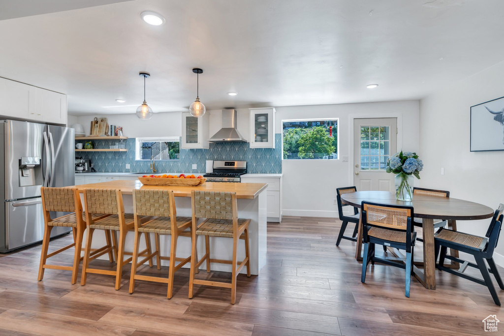 Kitchen with appliances with stainless steel finishes, wall chimney range hood, backsplash, white cabinetry, and glass insert cabinets