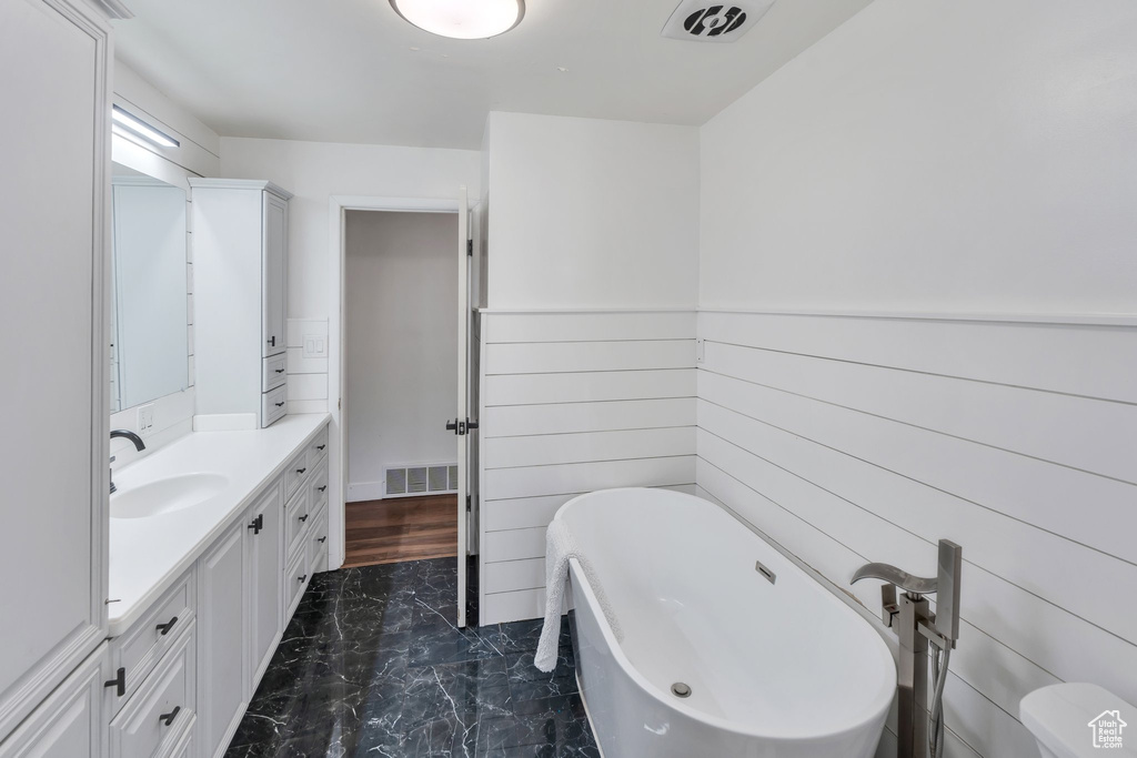 Full bath with marble look tiles, vanity, and a freestanding tub