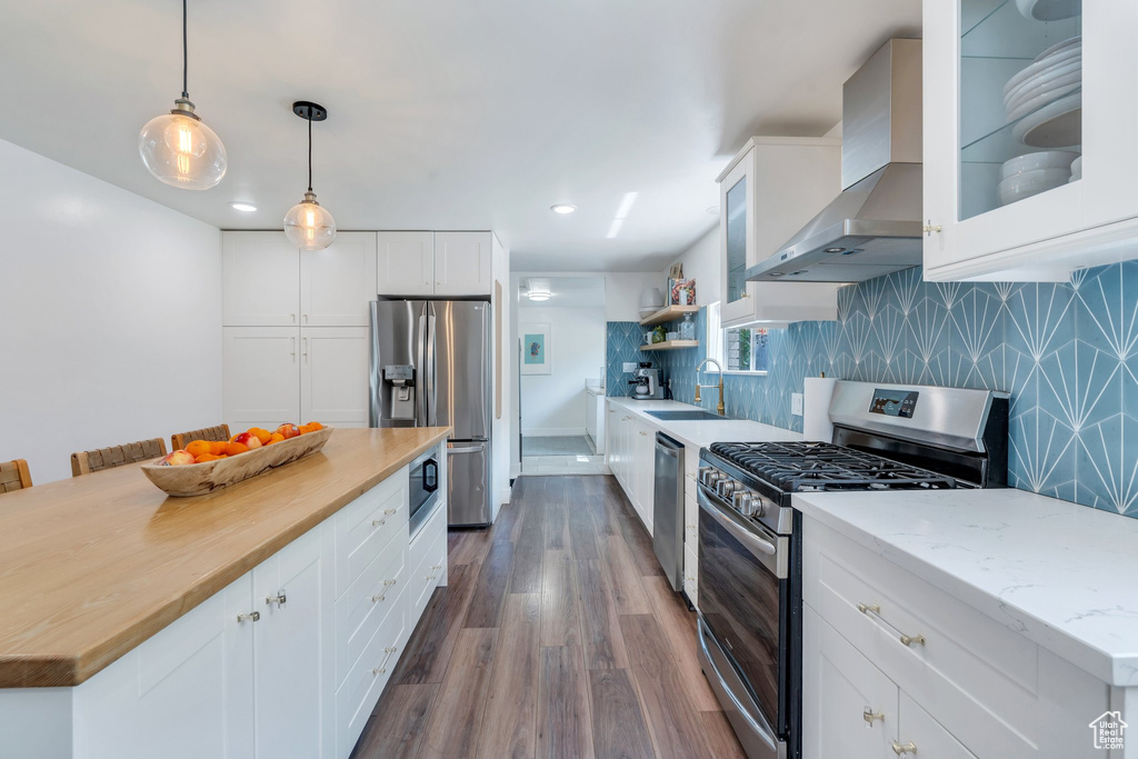 Kitchen with appliances with stainless steel finishes, wall chimney exhaust hood, dark wood finished floors, butcher block counters, and white cabinetry