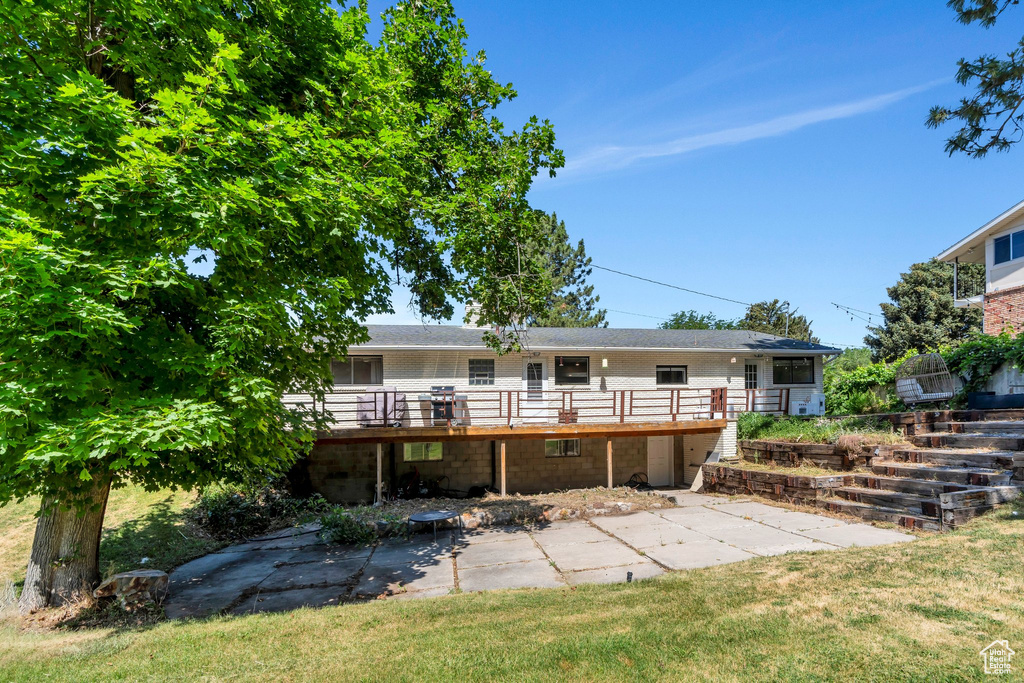 Back of property featuring a deck, a patio area, and a lawn