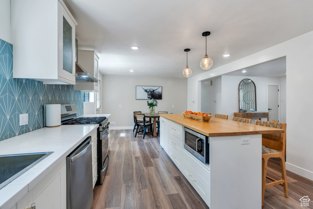 Kitchen featuring stainless steel appliances, wall chimney range hood, a kitchen bar, white cabinetry, and recessed lighting