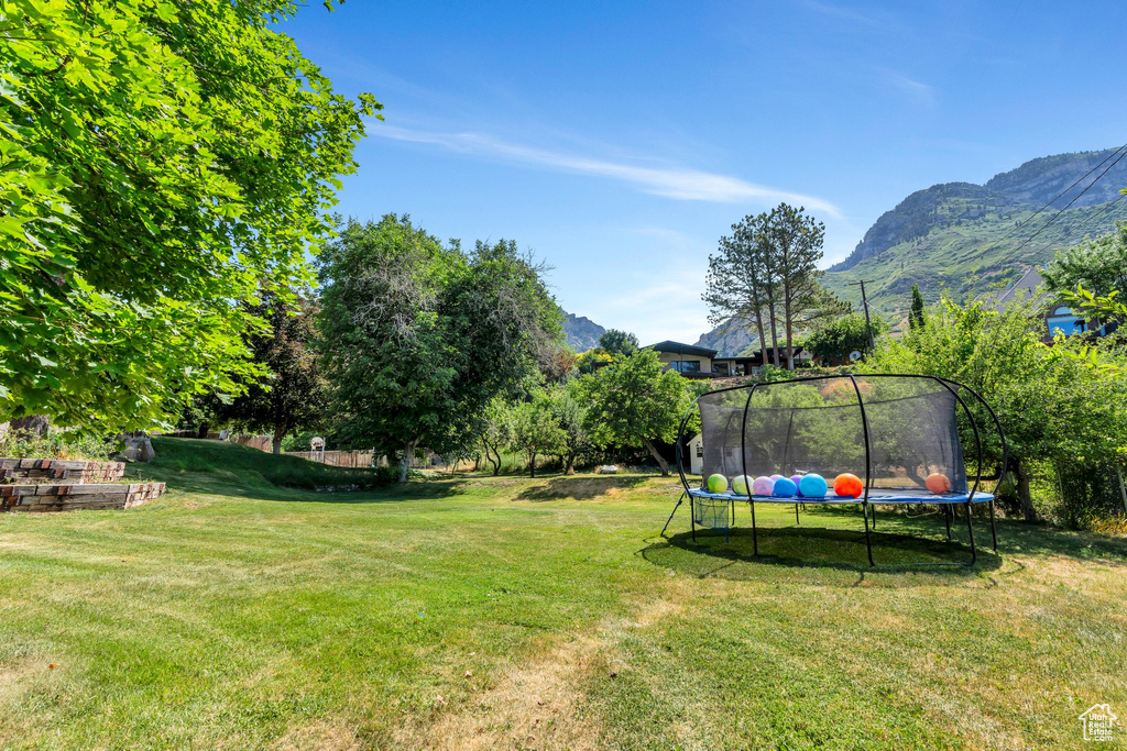 View of green lawn featuring a trampoline and a mountain view