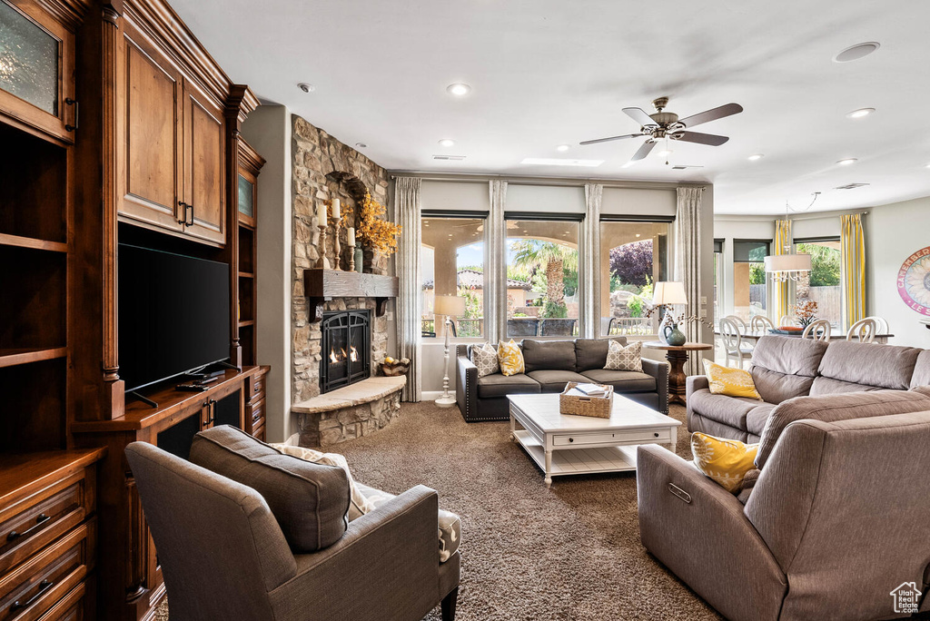 Living room with a stone fireplace, dark carpet, recessed lighting, and a ceiling fan