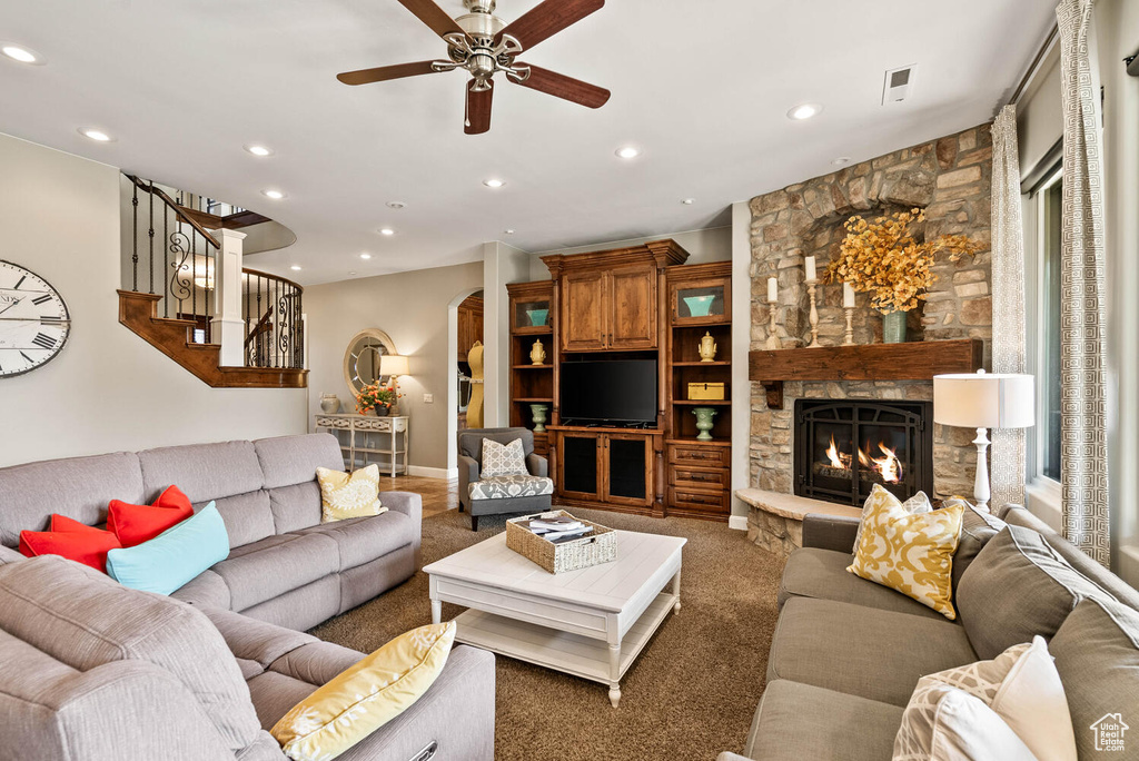 Carpeted living room with a ceiling fan, stairway, recessed lighting, and a stone fireplace