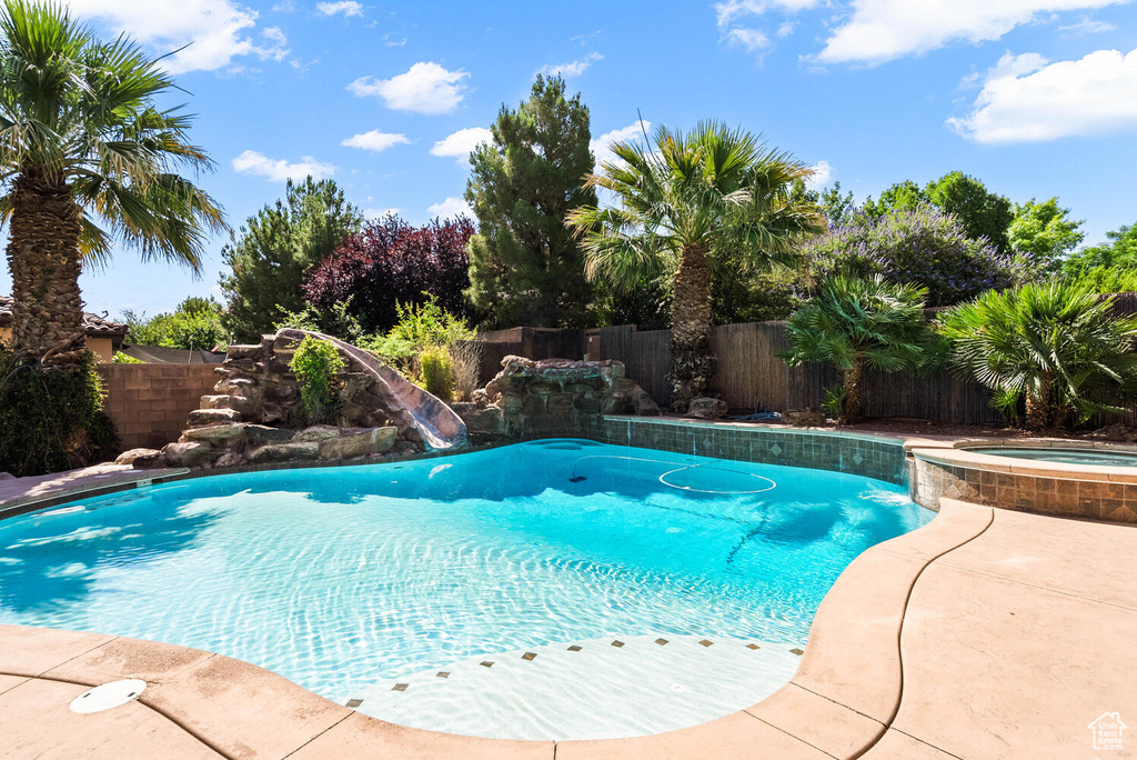 View of swimming pool with a water slide, a fenced backyard, and a pool with connected hot tub