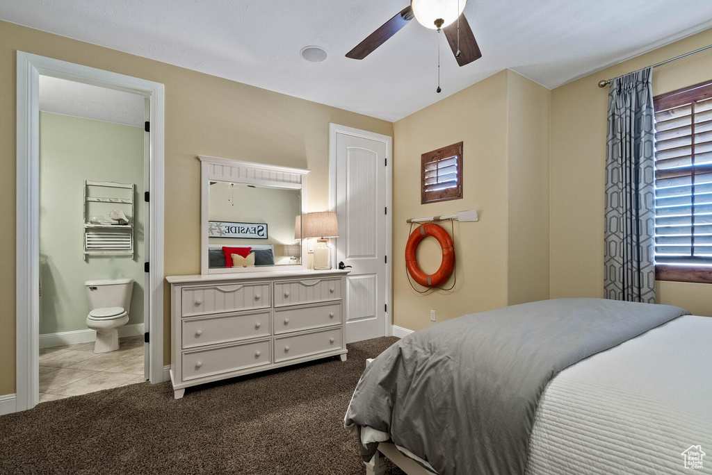 Bedroom with ensuite bath, dark colored carpet, and a ceiling fan